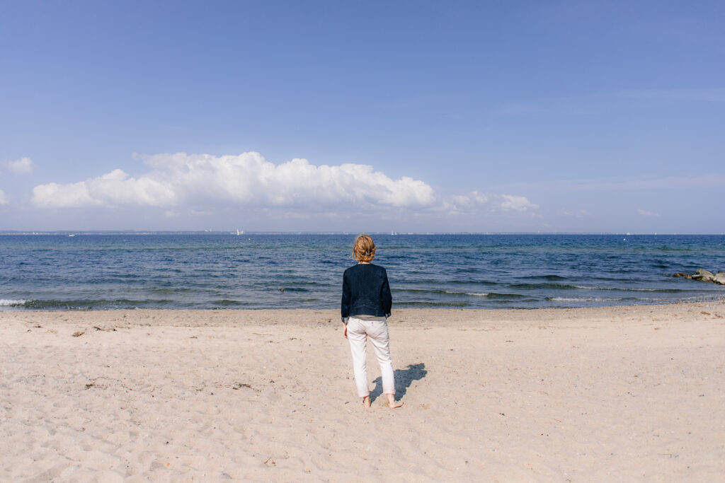 Frau am Strand mit dem Rücken zum Kamera gewandt, Blick aufs Mehr